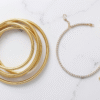 Bangle vs chain bracelet comparison on a white marble surface showing gold stacked bangles beside a diamond tennis bracelet