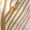Gold chain necklaces in Bahrain displayed on a white marble surface showing curb, rope, and Figaro chain styles